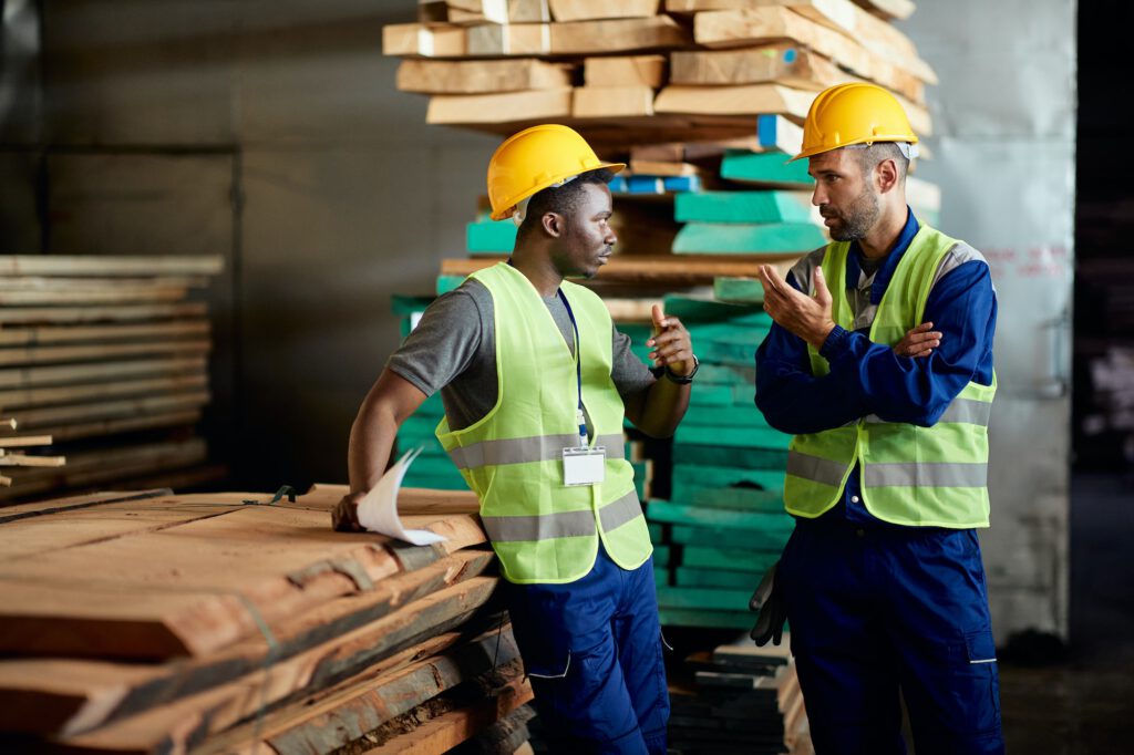 Male workers communicating while working at wood warehouse.