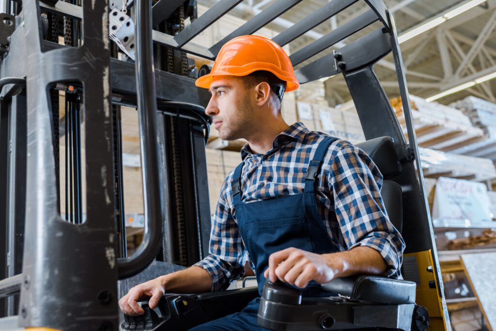 warehouse worker in uniform and helmet operating forklift machine